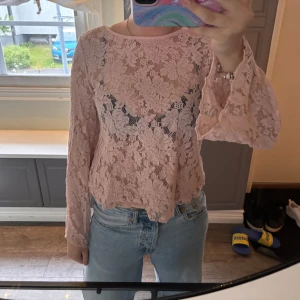 Ljusrosa spetsblus med blommönster - Säljer en ljusrosa blus i spets med blommigt mönster. Blusen har lång ärm och vackra detaljer med korsade band i nacken. Perfekt för en sommar fest 💞