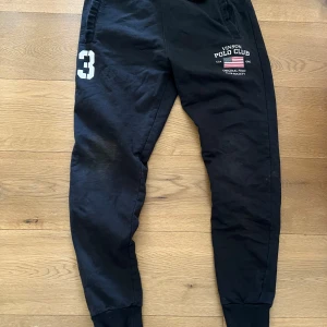 Svarta mjukisbyxor från Vinson Polo Club - Svarta mjukisbyxor från Vinson Polo Club med tryckt logga och siffran 3 på ena benet. Byxorna har resår i midjan och vid bensluten, samt sidofickor. Perfekta för en avslappnad stil.