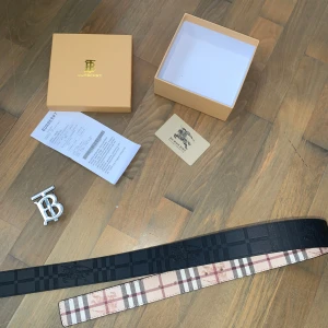 Burrberry belte reverseable - SELGER FRA NORGE KOSTER 450 NORSKE KRONER IKKE SVENSKE! Snyggt vändbart Burberry-bälte i skinn med klassiskt rutigt mönster i beige, rött, vitt och svart på ena sidan och helsvart med diskret rutmönster på andra. Stor silverfärgad BB-logga som spänne. Kommer med originalbox och certifikat.
