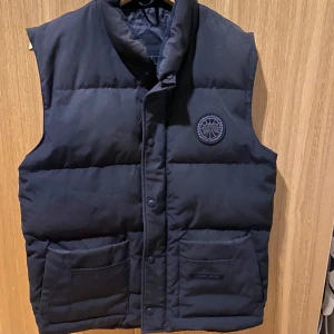 Canada Goose Freestyle Väst Black Label - Svart, stl M - Säljer en Canada Goose Freestyle Väst Black Label i färgen svart och storlek Medium. Västen är i bra skick och sparsamt använd - inga fläckar, hål eller skador.  Storlek: Medium Färg: Svart  Nypris ca 7500 kr Mitt pris: 3 000 kr