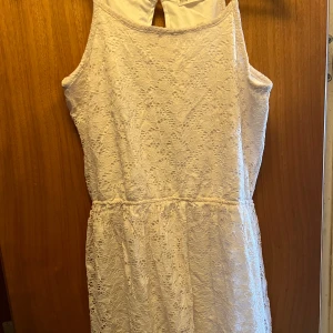 Vit spetsklänning från H&M - Säljer en söt vit spetsklänning från H&M med ärmlös design och öppen rygg. Klänningen har en mjuk spets över hela och en lätt utställd kjol. Perfekt för sommarens tillfällen eller studentfirande! (Barn)