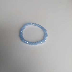 Blått glittrigt pärlarmband - Snyggt armband med små, facetterade pärlor i ljusblått som ger ett glittrigt intryck. Perfekt accessoar för att addera lite färg och shine till din outfit. Elastiskt band gör det enkelt att ta på och av.