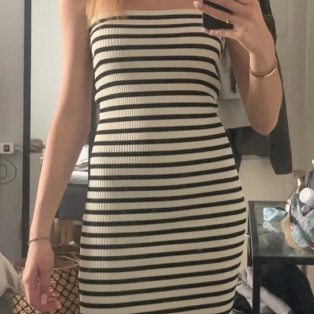 Snygg axelbandslös klänning med svartvita ränder. Den har en tight passform och är ribbad, vilket ger en stilren look. Perfekt för sommarens varma dagar.. Mekot.
