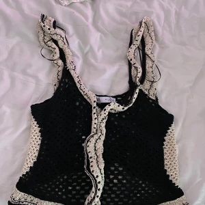Svart och vit virkad topp från Zara - Säljer en unik svart och vit virkad topp från Zara med volangdetaljer och knytning. Toppen har en vacker öppen design och är perfekt för sommardagar. Den är ärmlös och har en elegant look.