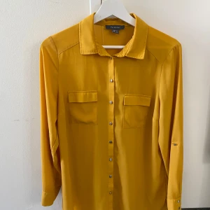 Gul långärmad skjorta från PRIMARK - Snygg gul skjorta från PRIMARK med långa ärmar och knappar framtill. Skjortan har två bröstfickor med lock och en klassisk krage. Perfekt för en färgglad stil. Har haft den i garderoben hur länge som helst och tagit ut den nu och den behövdes inte strykas för materialet är super fint.