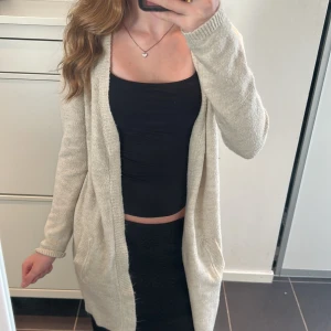 Beige stickad kofta - Mysig beige stickad kofta med långa ärmar och öppen design. Perfekt för kyliga dagar och enkel att matcha med olika outfits. Koftan har praktiska fickor framtill.