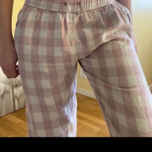 Rutig pyjamas byxa i rosa och vit - Säljer ett par bekväma pyjamas byxor med rutigt mönster i rosa och vitt. Byxorna har en elastisk midja för extra komfort och en avslappnad passform. Perfekta för en avslappnad dag hemma eller ute.