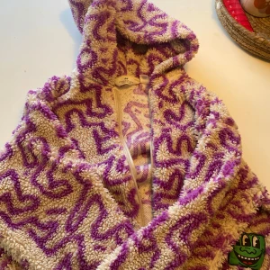 Lila och beige teddyjacka från H&M - Mysig teddyjacka från H&M i lila och beige med ett unikt mönster. Jackan har en dragkedja framtill och en huva för extra värme. Perfekt för kyliga dagar när du vill vara både bekväm och stilren.