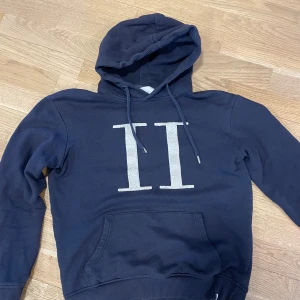 Mörkblå hoodie med tryck - Snygg mörkblå hoodie med stort vitt tryck på framsidan. Den har en klassisk känguruficka och justerbar huva med dragsko. Perfekt för en avslappnad stil.