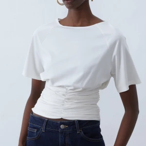 Vit kortärmad topp med rynkad midja - Vit topp med korta ärmar och en  rynkad detalj i midjan. 