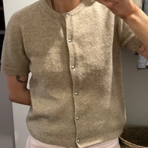 Beige kortärmad kofta - Säljer en stilren beige kofta med korta ärmar och knappar framtill. Knappt använd.