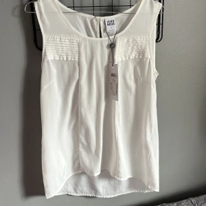 Vit ärmlös topp från Vero Moda - Säljer en stilren vit ärmlös topp från Vero Moda. Toppen har fina veckade detaljer på bröstet och en rund halsringning. 