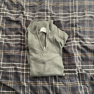 Grå halvsip från Bläck - Säljer en stilren grå tröja från Bläck med dragkedja vid halsen. Perfekt för en avslappnad look. Tröjan har långa ärmar och är tillverkad i ett mjukt material.