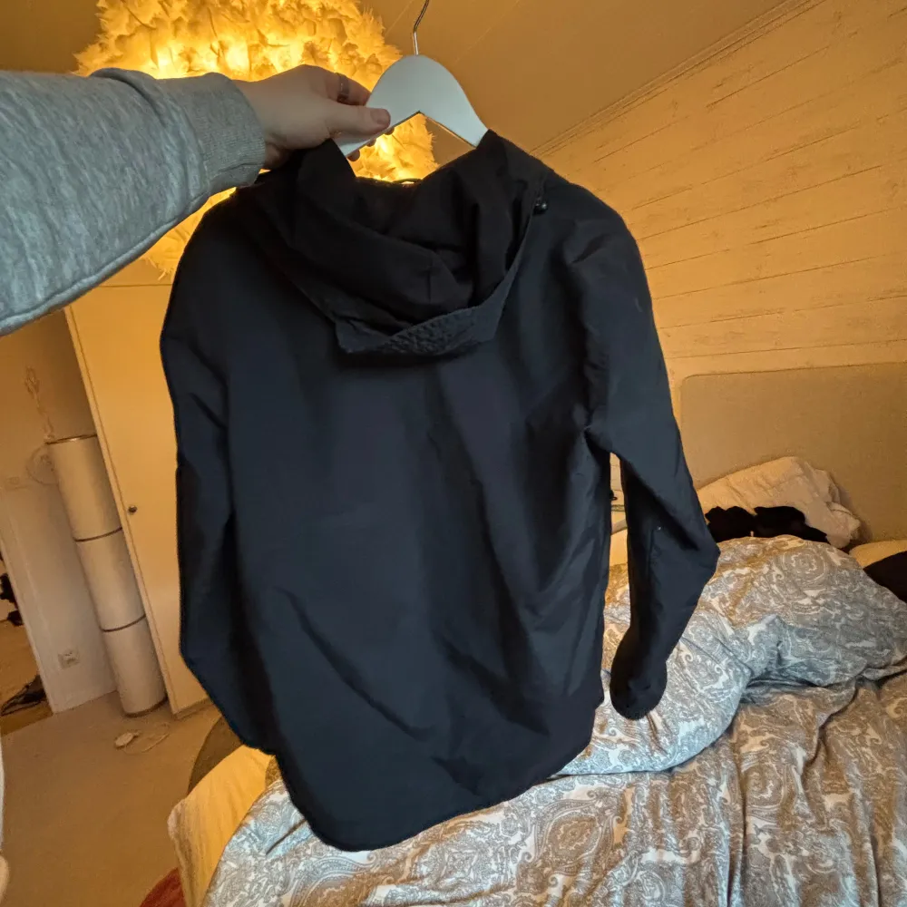 Snygg svart jacka från Lyle & Scott med dragkedja och huva. Perfekt för kyligare dagar. Jackan har långa ärmar och elastiska muddar för extra komfort. Den klassiska loggan syns på bröstet.. Takit.