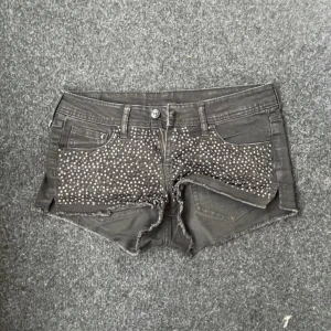 H&M Krystal shorts - Snygga svarta jeansshorts från H&M med coola nitar framtill. De har en låg midja och fransiga kanter som ger en avslappnad look. Perfekta för en somrig dag eller en utekväll. Dragkedja och knapp framtill för enkel stängning.