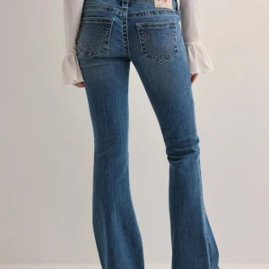 Blå bootcut jeans från True Religion - Snygga blå bootcut jeans från True Religion med klassisk femficksdesign och märkets ikoniska broderi på bakfickorna. Jeansen har en låg midja och stängs med knapp och dragkedja. 