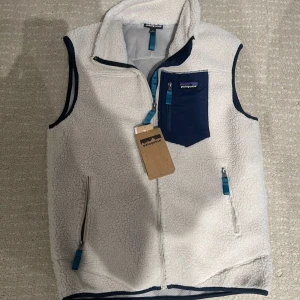  Patagonia fleece vest  - Säljer en snygg vit fleeceväst från Patagonia med marinblå detaljer. Västen har dragkedja fram och en praktisk bröstficka med dragkedja. Perfekt för lager-på-lager under kyliga dagar. 🏔️