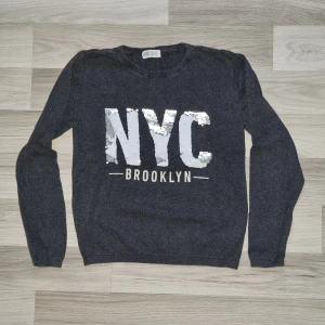 Grå tröja med paljetter från H&M - Säljer en snygg grå tröja från H&M med paljetter som bildar texten 'NYC Brooklyn' på framsidan. Tröjan har långa ärmar och en bekväm passform. Perfekt för en cool och avslappnad stil. 🗽✨