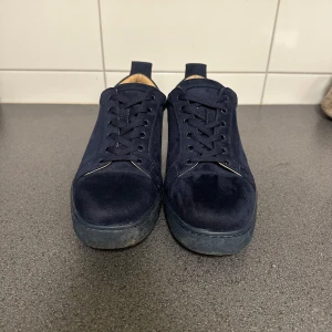 Mörkblå sneakers med röd sula - Snygga mörkblå sneakers i mocka med klassisk röd sula. Skorna har snörning och en rund tå, vilket ger en stilren look. Perfekta för dig som vill ha en stilren och modern stil.