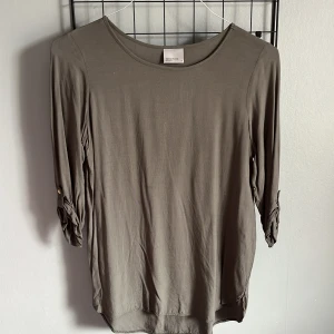 Olivgrön topp från Vero Moda - Säljer en stilren olivgrön topp från Vero Moda. Toppen har trekvartsärmar med knappdetalj och en rund halsringning. 