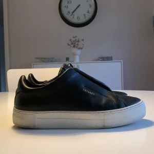 Svarta sneakers från Axel Arigato - Snygga svarta sneakers från Axel Arigato i skinn med vit sula. Dom är i bra skick!