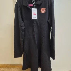 Svart klänning från Monki XS  - Säljer en svart långärmad klänning från Monki med en söt broderad gris på bröstet. Klänningen är tillverkad i 100% bomull. Helt ny med prislapp kvar. 