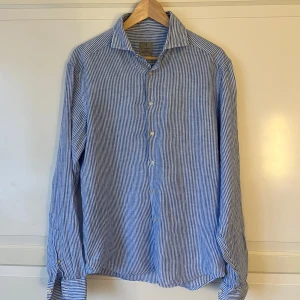 Blå och vit randig skjorta från La Chemise - Snygg blå och vit randig skjorta från La Chemise i storlek 39. Skjortan har en klassisk krage och knappar framtill. Linne material och perfekt inför sommaren. Vid frågor & funderingar är det bara att höra av sig! NYPRIS: 900kr