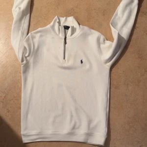 Polo Ralph Lauren Quarter-Zip - Säljer en vit quarter-zip från Ralph Lauren med  det klassiska logotypbroderiet i blått på bröstet. Tyvärr så har den fläck på sig (parfym fläck) men det går att lösa i tvättmaskinen. Priset kan diskuteras vid snabb affär. Storleken är S.