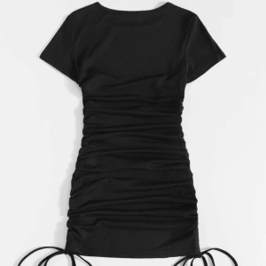 Svart ribbad klänning från Shein - Snygg svart ribbad klänning från Shein med korta ärmar och knytband i sidorna för justerbar längd. Perfekt för en stilren look. Klänningen har en åtsittande passform som framhäver figuren.