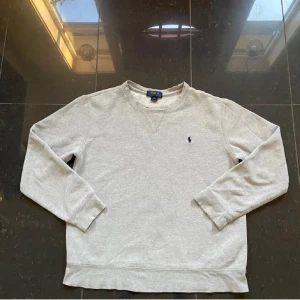 STEALL!!!! Raffe tröja - Säljer en stilren grå tröja från Polo Ralph Lauren med lång ärm och rund halsringning. Tröjan har en liten broderad logotyp på bröstet. Perfekt för en avslappnad och klassisk look. Storlek: L i barnstorlek vilket motsvarar XS/14-16. Skulle rekomenderas att vara 170 cm lång om tröjan ska användas till bruk.