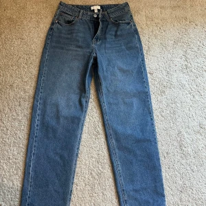 Blå jeansbyxor - Snygga blå jeansbyxor med klassisk femficksdesign och knappgylf. Perfekta för en avslappnad stil. Passformen är rak och de har en traditionell midjehöjd.