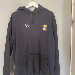 Svart hoodie med BOIS-logga - Säljer en svart hoodie med BOIS-logga och nummer 34 på bröstet. Den har en klassisk känguruficka och justerbar huva med dragsko. Perfekt för en avslappnad stil.