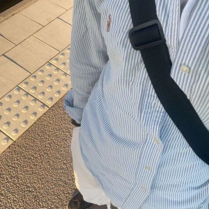 Blå- och vitrandig ralph lauren skjorta - Snygg blå- och vitrandig skjorta med knappar framtill. Skjortan har en klassisk krage och långa ärmar, perfekt för en stilren look. Passar bra till både jeans och chinos.