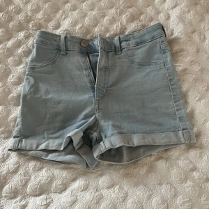 Ljusblå jeansshorts - Snygga ljusblå jeansshorts med upprullade ben och klassisk femficksdesign. Perfekta för sommardagar och avslappnade stunder. De har en knapp och dragkedja framtill för enkel på- och avtagning. 