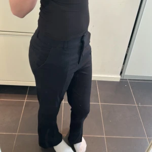 Svarta kostymbyxor - Snygga svarta kostymbyxor med mid waste och rak passform. Perfekta för en stilren look. Byxorna har diskreta fickor och en klassisk design.