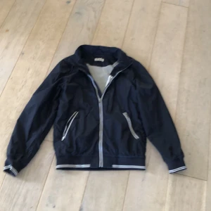 Mörkblå vindjacka  - Säljer en fet vindjacka som är perfekt nu på våren! Den är i fint skick och går enkelt att matcha med. Den är i storlek S och luva följer även med! Det är en luva som är avtagbar och knapparna syns inte om man inte har luvan!