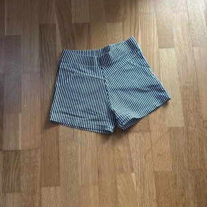 Randiga shorts - Säljer ett par snygga randiga shorts i blått och vitt. De har en normal passform och är perfekta för sommardagar. Shortsen har praktiska fickor och en bekväm midja.