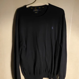 Svart tröja från Ralph Lauren - Säljer en stilren svart tröja från Ralph Lauren i slim fit. Tröjan är tillverkad i mjuk pima bomull och har en broderad logga på bröstet. Perfekt för en klassisk look. Storleken är L men passar även M, nypriset på denna är ca 1000