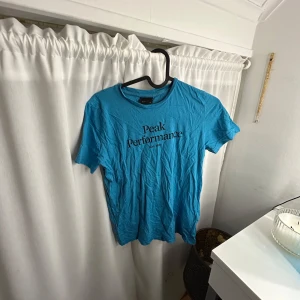 Blå t-shirt från Peak Performance - Säljer en blå t-shirt från Peak Performance med tryck på framsidan. T-shirten har en normal passform och är kortärmad, perfekt för vardagsbruk. Tillverkad i ett mjukt material för extra komfort.