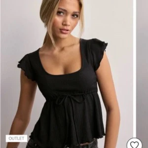 Svart blus från Nelly - Säljer en svart blus från Nelly med korta volangärmar och knytband i midjan. Perfekt för en stilren look.