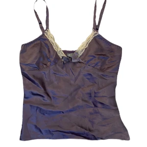 Lila satinpyjamas med spetsdetaljer - Säljer ett elegant lila satinpyjamas sett. Linnet har  justerbara axelband och vacker spetsdetalj vid halsringningen. Linnet har även en liten rosett framtill som ger en extra touch av stil. Byxorna har spets detalj längst ner. Ett extremt bekvämt och gulligt sett!! Pris kan diskuteras :)