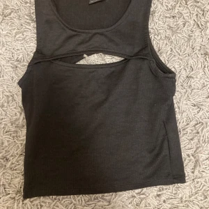 Svart ribbad linnetopp - Snygg svart ribbad linnetopp med ett unikt utskuret mönster på ryggen. Perfekt för en stilren och modern look. Passar bra till både jeans och kjol.