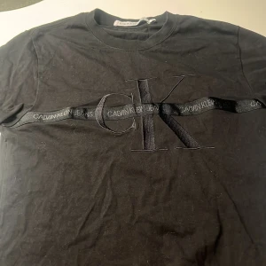 Svart t-shirt från Calvin Klein Jeans - Snygg svart t-shirt från Calvin Klein Jeans med ett stort CK-logotyp tryck över bröstet. T-shirten har en rund halsringning och korta ärmar. Perfekt för en stilren och avslappnad look.