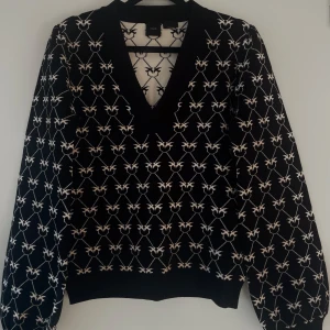 Svart stickad tröja med mönster - Säljer en svart stickad tröja med ett unikt vitt mönster. Tröjan har en v-ringad hals och långa ärmar, perfekt för kyligare dagar. Den är både stilren och bekväm.