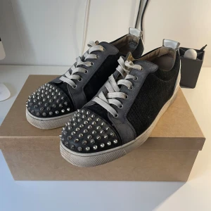 Christian Louboutin svarta sneakers med nitar - Svarta sneakers från Christian Louboutin med grå detaljer och vita snören. Några nitar har gått av men extra medföljer. Allt OG ingår, box, dustbag, etc. Kan garantera skornas äkthet också!