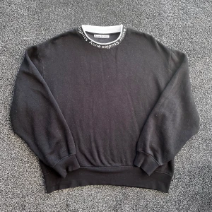 Acne Studios sweatshirt - Svart sweatshirt från Acne Studios med vit och svart ribbad krage där Acne Studios-loggan är broderad runt om. Tröjan har lång ärm, loose passform och är tillverkad i mjuk bomull. Perfekt för dig som gillar stilrena och cleana plagg med diskret branding. Storlek M, skick 9/10, pris går att diskutera✅