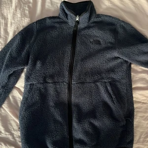 Blå teddyjacka från The North Face M - Mysig blå teddyjacka från The North Face i storlek M. Jackan är tillverkad i 100% polyester, har hel dragkedja framtill, höga fickor och broderad logga på bröstet. 