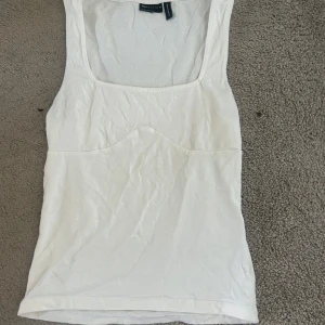 Vit linnetopp  - Fräsch vit linnetopp från ASOS med fyrkantig urringning och sömdetalj under bysten. Modellen är ärmlös och har en clean, enkel look som funkar till jeans eller kjol. Mjukt bomullsmaterial som känns skönt mot huden.