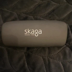 Svart glasögonfodral från Skaga - Stilrent svart glasögonfodral från Skaga, Sweden 1948. Utsidan är matt svart med vit logotyp och insidan är ljus med klassisk Skaga-stämpel. Perfekt för att skydda dina glasögon med en clean och tidlös look.