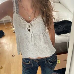 Vit spetsdetaljerad linnetopp - Supersöt vit linnetopp med spetskantade axelband och knytning framtill från Gina tricot. Toppen har en lätt skrynklig struktur och är ärmlös med en luftig, flowy passform. Perfekt för varma dagar och ger en romantisk vibe.mycket bra skick, hör av dig om du har frågor eller funderingar 💕